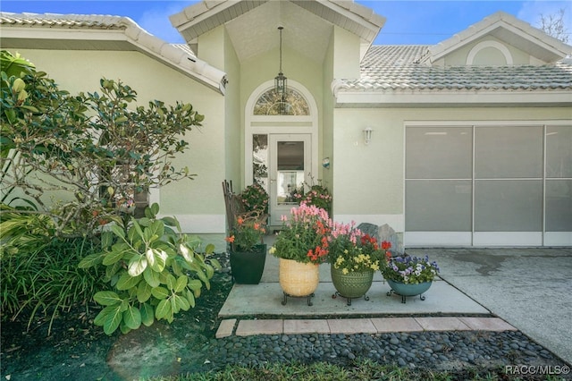 view of exterior entry featuring stucco siding, concrete driveway, and a tiled roof