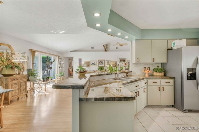 kitchen featuring a peninsula, a sink, decorative backsplash, vaulted ceiling, and stainless steel fridge