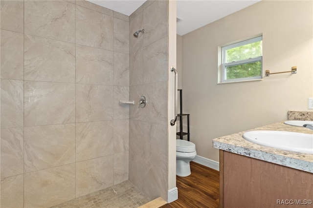 bathroom with hardwood / wood-style flooring, vanity, toilet, and a tile shower