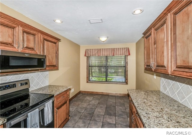 kitchen with backsplash, light stone counters, dark tile patterned flooring, and appliances with stainless steel finishes