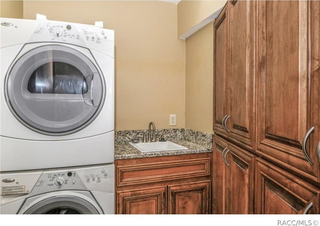 laundry room featuring sink, cabinets, and stacked washer and clothes dryer