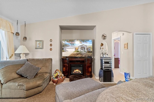 interior space featuring light carpet, baseboards, arched walkways, and a glass covered fireplace