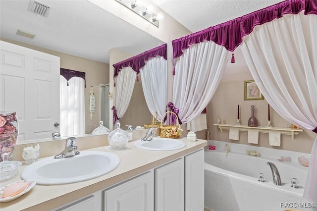 bathroom with a garden tub, a textured ceiling, a sink, and visible vents