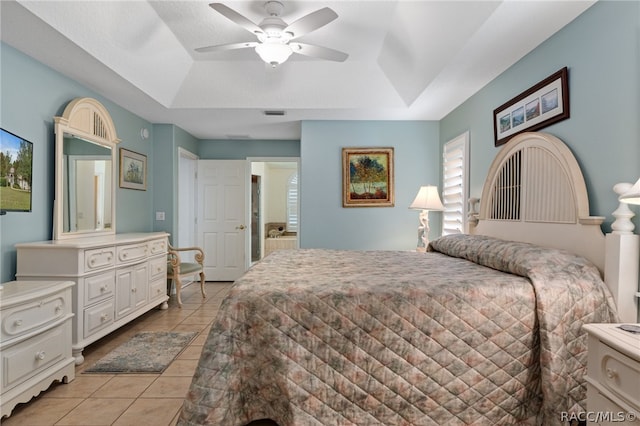 tiled bedroom with ceiling fan, connected bathroom, and a tray ceiling