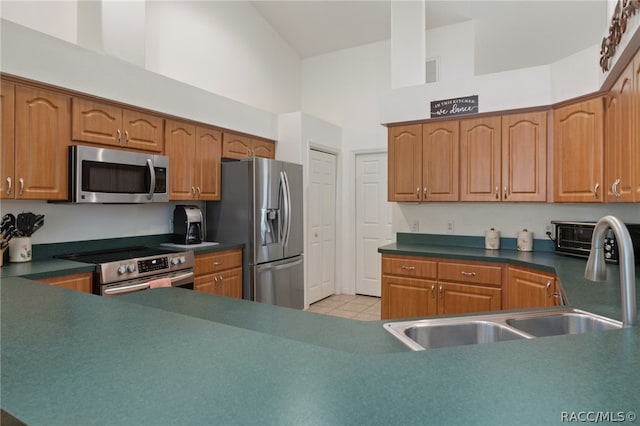 kitchen with sink, a towering ceiling, and appliances with stainless steel finishes