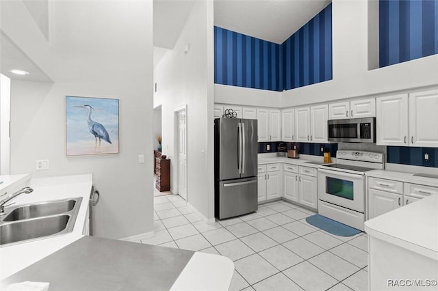 9989 N Langdon Rd, Citrus Springs, FL 34434 - kitchen with appliances with stainless steel finishes, a high ceiling, white cabinetry, wallpapered walls, and light tile patterned flooring