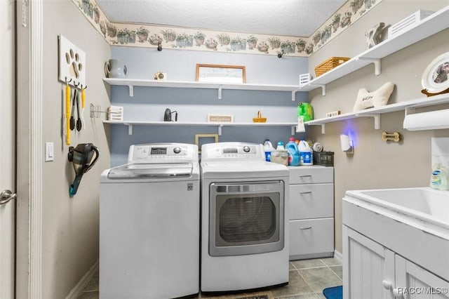 laundry room featuring a textured ceiling, light tile patterned floors, a sink, cabinet space, and washing machine and clothes dryer