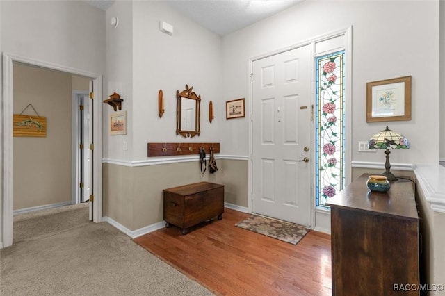 foyer with carpet floors, baseboards, and wood finished floors