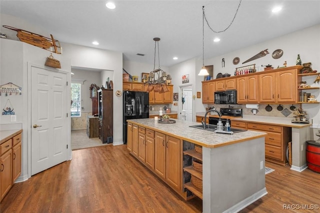 kitchen featuring a sink, light countertops, black appliances, open shelves, and a center island with sink