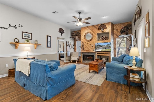 living room featuring wood walls, a fireplace, wood finished floors, visible vents, and a ceiling fan