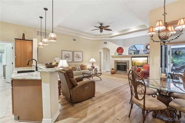 dining space with visible vents, a tray ceiling, light wood-style flooring, a tile fireplace, and arched walkways