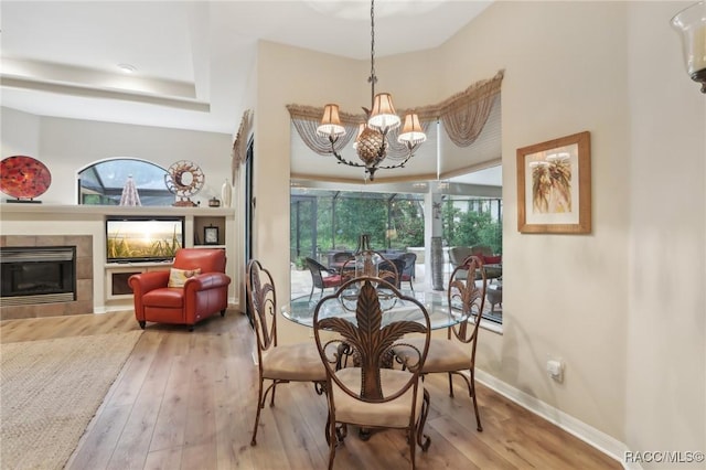 dining space featuring a tiled fireplace, a notable chandelier, baseboards, and hardwood / wood-style floors