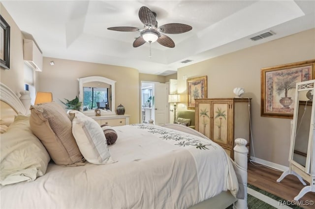 bedroom with a tray ceiling, wood finished floors, visible vents, and baseboards