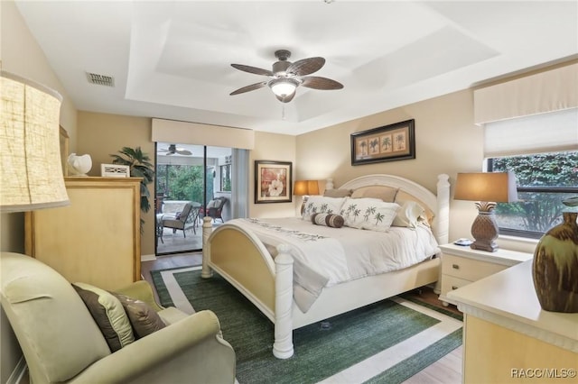 bedroom with access to exterior, visible vents, ceiling fan, a tray ceiling, and wood finished floors