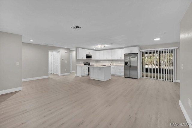 kitchen with stainless steel appliances, a kitchen island, white cabinets, open floor plan, and light countertops