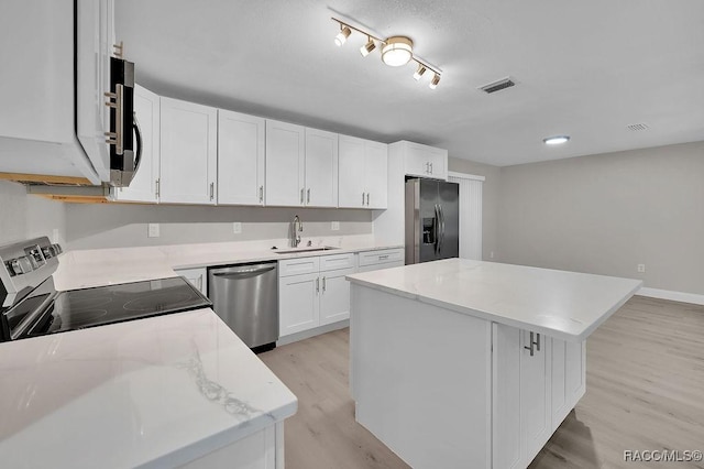 kitchen with white cabinets, light wood-style flooring, a kitchen island, stainless steel appliances, and a sink