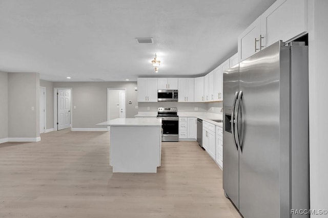 kitchen with stainless steel appliances, light countertops, light wood-style flooring, white cabinets, and a kitchen island