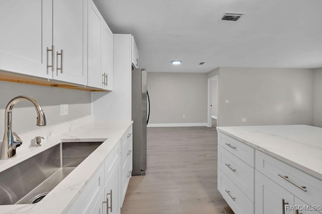 kitchen featuring light stone counters, a sink, freestanding refrigerator, and white cabinets