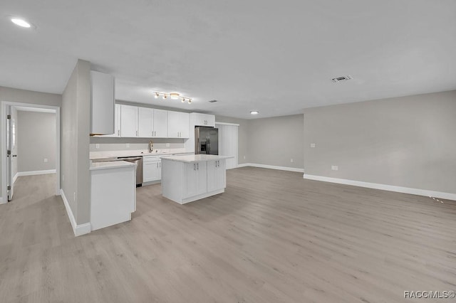 kitchen featuring stainless steel appliances, light countertops, open floor plan, white cabinetry, and a kitchen island