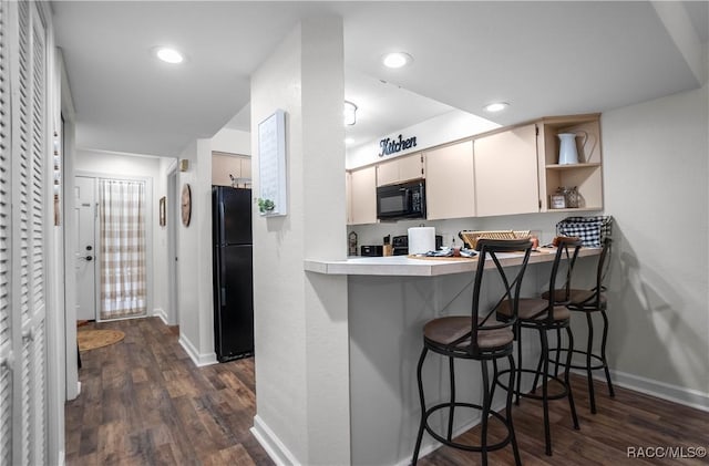 kitchen with dark wood-type flooring, a breakfast bar area, kitchen peninsula, and black appliances