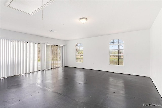 spare room with attic access, baseboards, visible vents, and finished concrete floors