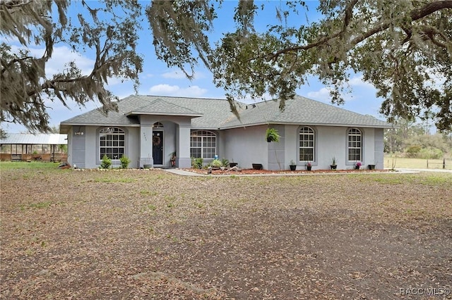 ranch-style home featuring stucco siding and roof with shingles