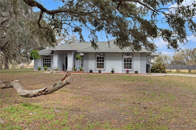 ranch-style house featuring a front yard, roof with shingles, and stucco siding