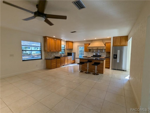 kitchen featuring a center island, a healthy amount of sunlight, a kitchen breakfast bar, appliances with stainless steel finishes, and custom exhaust hood