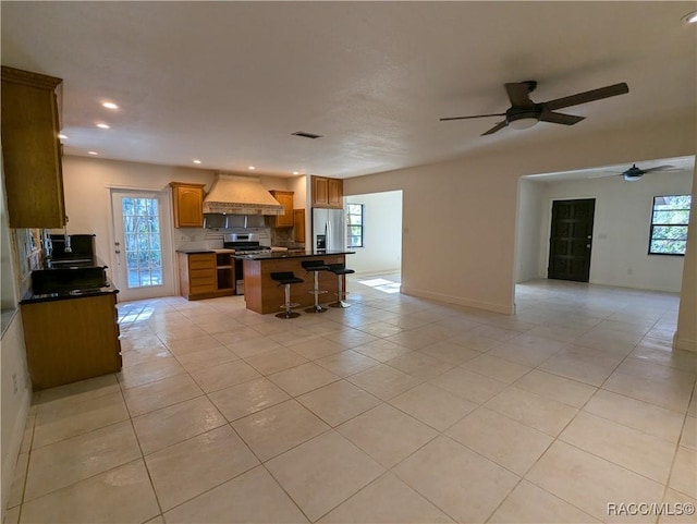 kitchen featuring custom exhaust hood, a center island, a kitchen breakfast bar, light tile patterned floors, and stainless steel appliances