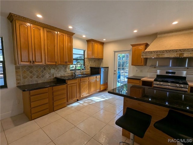 kitchen with premium range hood, dark stone counters, stainless steel appliances, sink, and light tile patterned floors