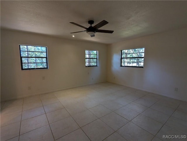 empty room with ceiling fan, light tile patterned floors, and a wealth of natural light