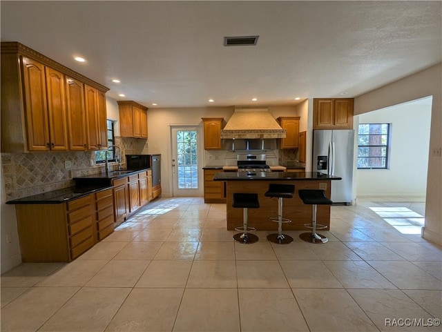 kitchen featuring premium range hood, stainless steel appliances, sink, light tile patterned floors, and a center island