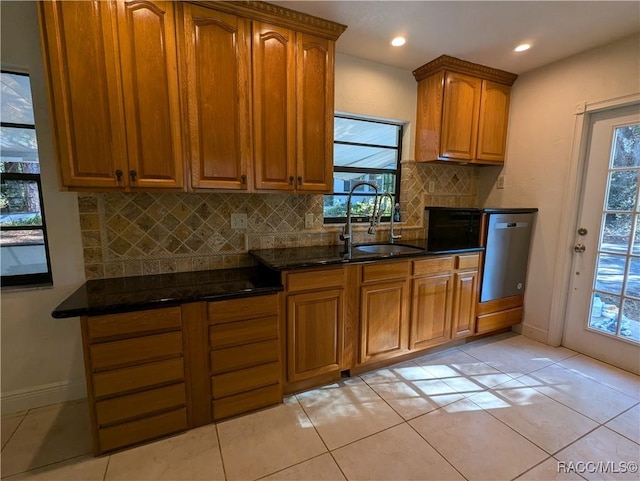 kitchen with dark stone counters, sink, stainless steel dishwasher, light tile patterned floors, and tasteful backsplash