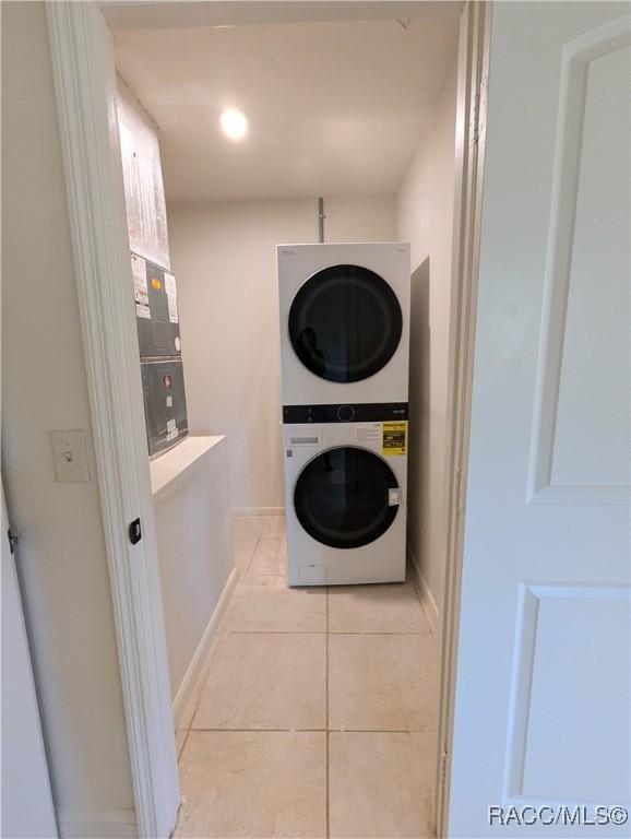 laundry area with stacked washing maching and dryer and light tile patterned flooring