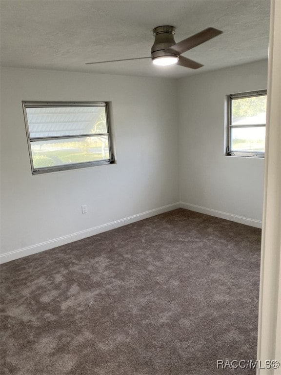 empty room with dark colored carpet, ceiling fan, and a textured ceiling