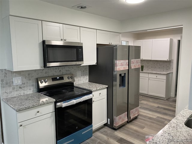 kitchen with light stone countertops, appliances with stainless steel finishes, tasteful backsplash, hardwood / wood-style flooring, and white cabinets