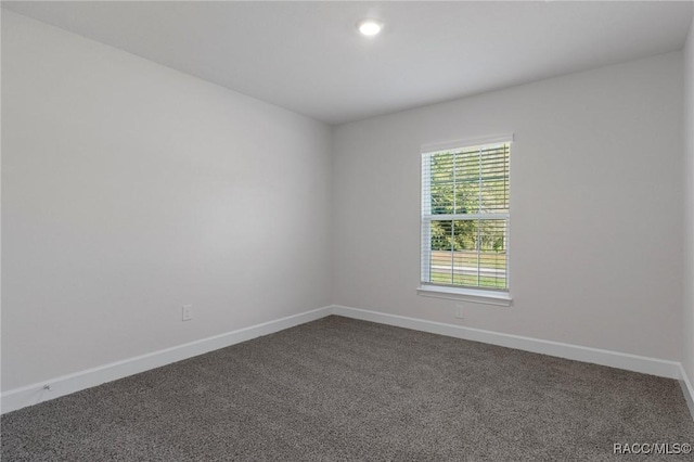 empty room featuring baseboards and dark colored carpet