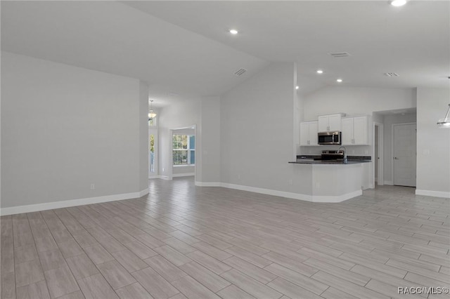 unfurnished living room with vaulted ceiling, recessed lighting, baseboards, and light wood-type flooring