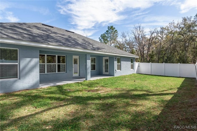 back of house featuring stucco siding, a lawn, a fenced backyard, roof with shingles, and a patio area