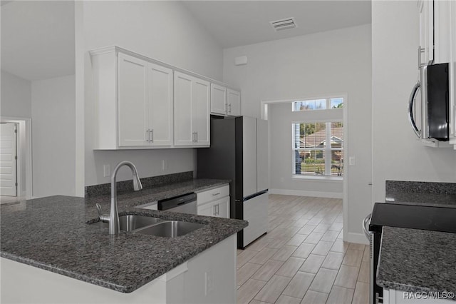 kitchen with a sink, white cabinetry, dark stone counters, appliances with stainless steel finishes, and a peninsula