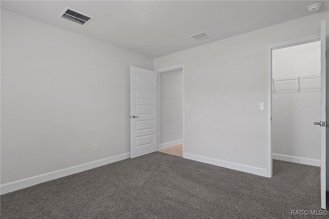 unfurnished bedroom with a walk in closet, carpet flooring, baseboards, and visible vents