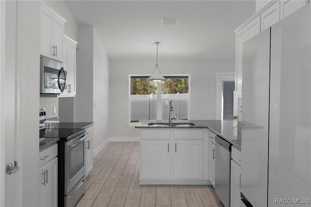 kitchen with wood tiled floor, a peninsula, stainless steel appliances, white cabinetry, and a sink