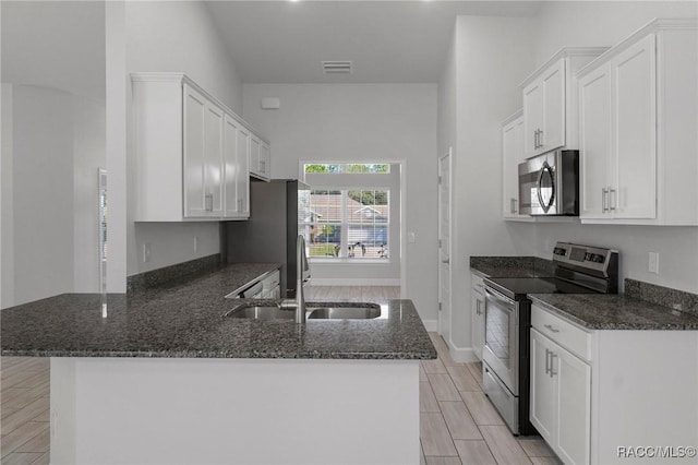 kitchen with visible vents, a peninsula, stainless steel appliances, and dark stone counters