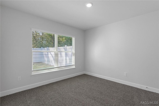 unfurnished room featuring baseboards and dark colored carpet