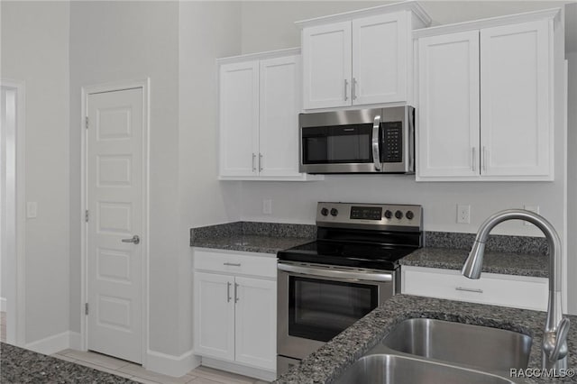 kitchen with dark stone counters, white cabinets, appliances with stainless steel finishes, and a sink