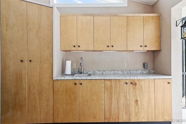 kitchen with light stone counters, sink, and light brown cabinets