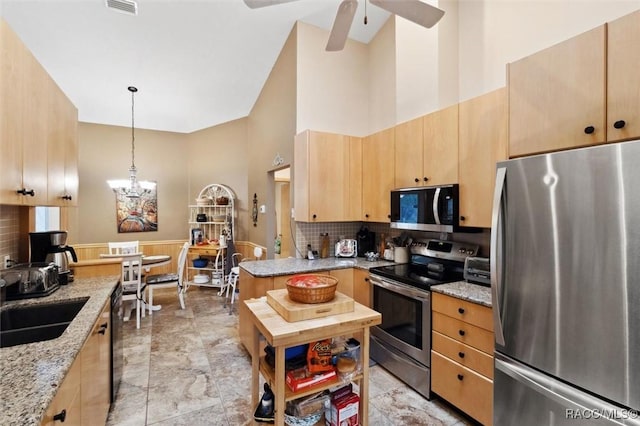 kitchen with stainless steel appliances, high vaulted ceiling, light stone countertops, decorative light fixtures, and light brown cabinets