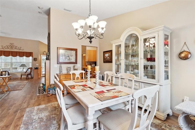 dining area with a chandelier, vaulted ceiling, and light wood-type flooring