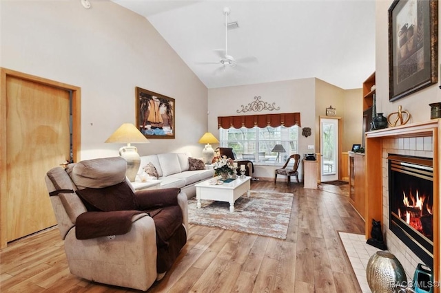 living room featuring a tiled fireplace, ceiling fan, high vaulted ceiling, and light hardwood / wood-style floors