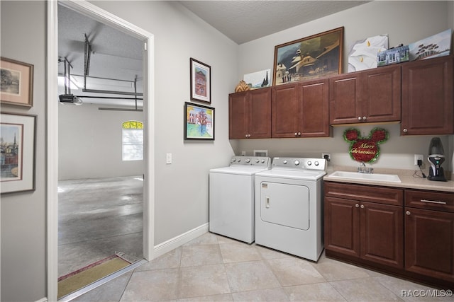 clothes washing area with cabinets, sink, washer and dryer, light tile patterned floors, and a textured ceiling